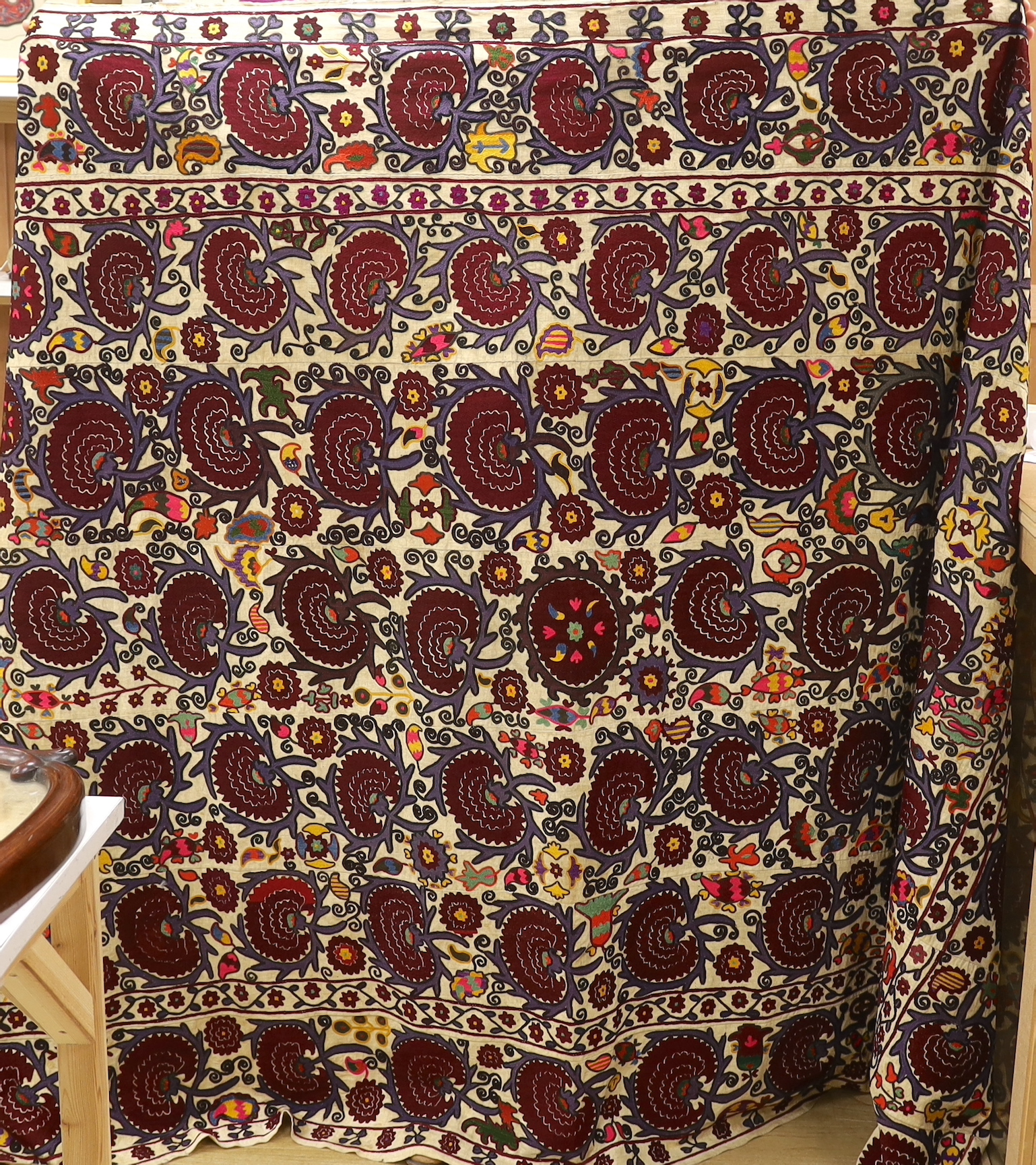 An exceptionally large Suzani hanging, embroidered with rows of stylised aubergine flower heads, the field filled with further polychrome flowers and serrated edged leaves, 190 x 270cm